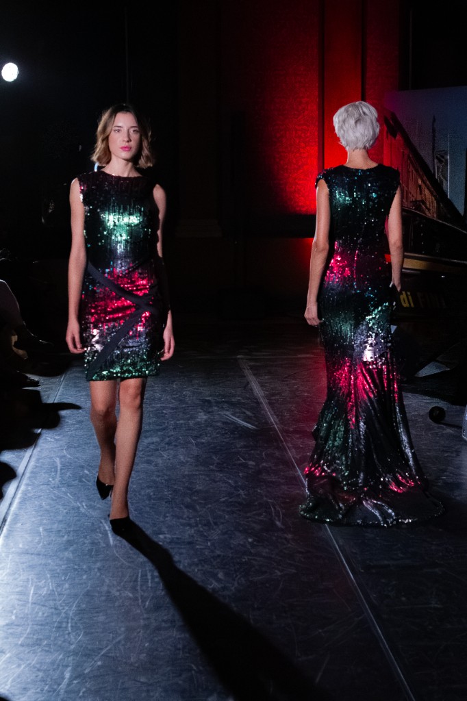 Due modelle in abiti lunghi ricoperti di paillettes verdi e magenta, in passerella con faretto laterale.