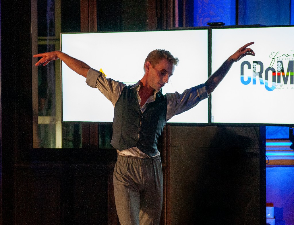 Danzatore in abito elegante sul palco davanti alle grandi schermate luminose con grafiche CROMATICA Festival.