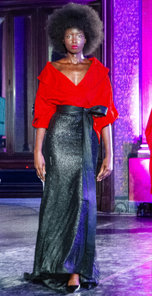 Modella in top rosso voluminoso e gonna lunga scintillante, acconciatura afro, passerella illuminata.
