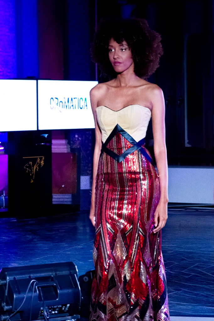 Modella in lungo abito con ricami metallici in passerella, sullo sfondo schermo con logo CROMATICA.