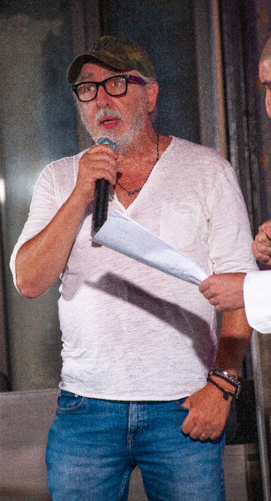 Relatore con cappello mimetico e camicia bianca che interviene al microfono durante l’evento del 21 settembre.