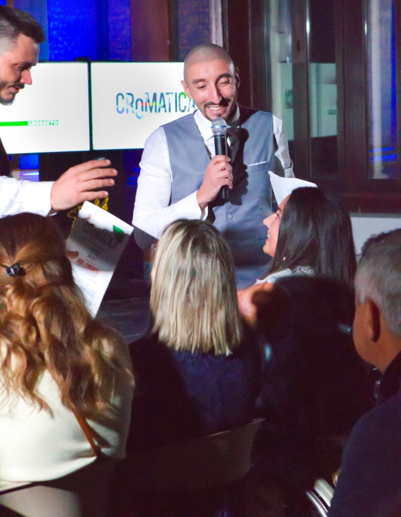 Relatore al microfono durante un incontro pubblico con schermi CROMATICA e riferimenti al territorio di Grosseto.